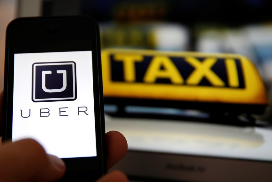 File illustration picture showing the logo of car-sharing service app Uber on a smartphone next to the picture of an official German taxi sign in Frankfurt, September 15, 2014. A Frankfurt court earlier this month instituted a temporary injunction against Uber from offering car-sharing services across Germany. San Francisco-based Uber, which allows users to summon taxi-like services on their smartphones, offers two main services, Uber, its classic low-cost, limousine pick-up service, and Uberpop, a newer ride-sharing service, which connects private drivers to passengers - an established practice in Germany that nonetheless operates in a legal grey area of rules governing commercial transportation. REUTERS/Kai Pfaffenbach/Files (GERMANY - Tags: BUSINESS EMPLOYMENT CRIME LAW TRANSPORT)